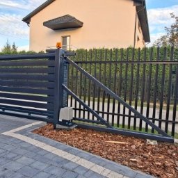 DaMet Damian Napora - Nowoczesna, przesuwna brama wjazdowa z automatyką, w kolorze grafitowym, z poziomymi panelami, na tle domu jednorodzinnego i ogrodzenia palisadowego.