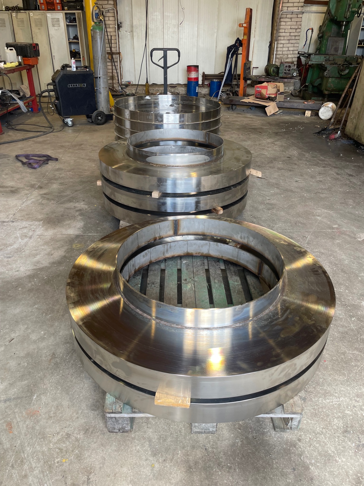 Polerowane, spawane pierścienie ze stali na paletach w warsztacie ślusarskim. Widoczne spawy i obróbka metalu. Elementy konstrukcyjne.