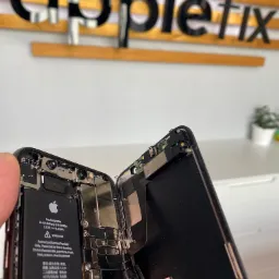 Rozłożony iPhone z widoczną baterią i wewnętrznymi komponentami, na tle logo serwisu Applefix.