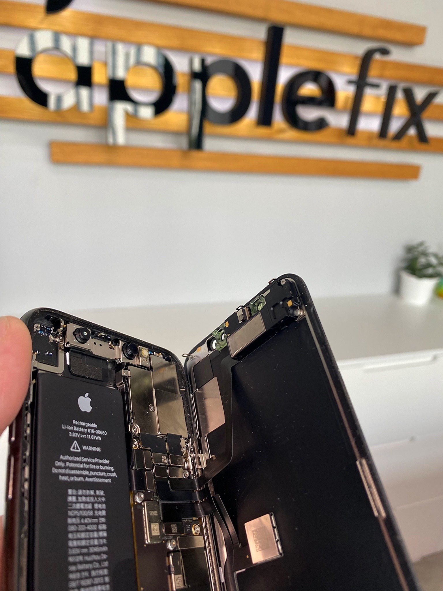 Rozłożony iPhone z widoczną baterią i wewnętrznymi komponentami, na tle logo serwisu Applefix.