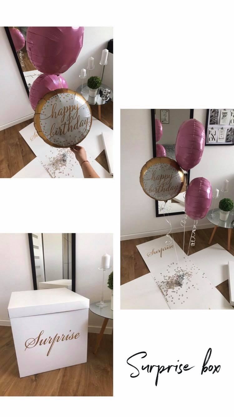 Kompozycja prezentowa: białe pudełko z napisem 'Surprise', balony w kolorze fuksji i złoty balon z napisem 'Happy Birthday', konfetti w środku pudełka.