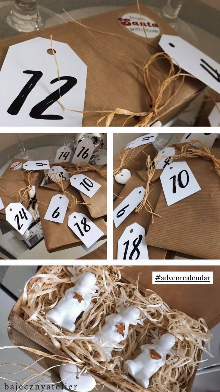 Ręcznie robiony kalendarz adwentowy z numerowanymi prezentami w brązowym papierze i małymi ceramicznymi figurkami aniołków w drewnianym pudełku wypełnionym siankiem.