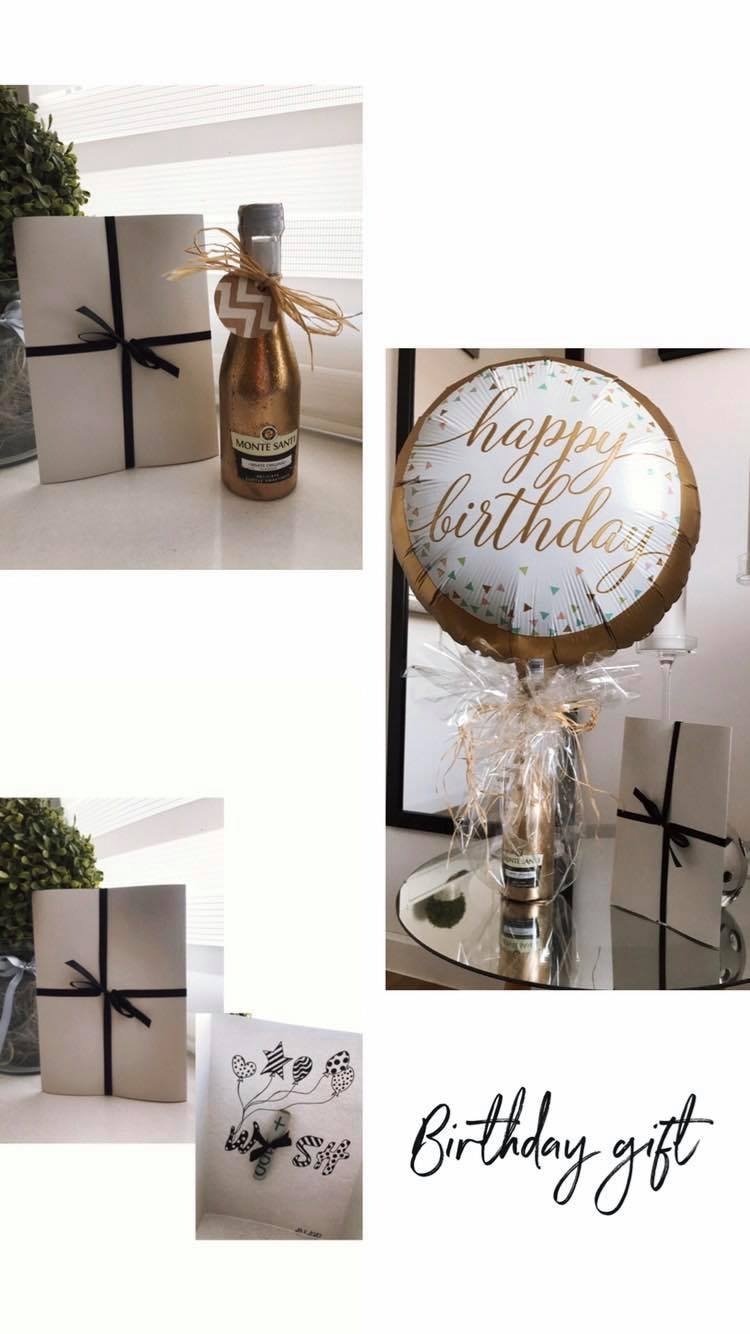 Zestaw prezentowy na urodziny: mini butelka wina musującego w złotej folii z rafii, pudełko prezentowe z czarną wstążką i balon z napisem 'Happy Birthday'.