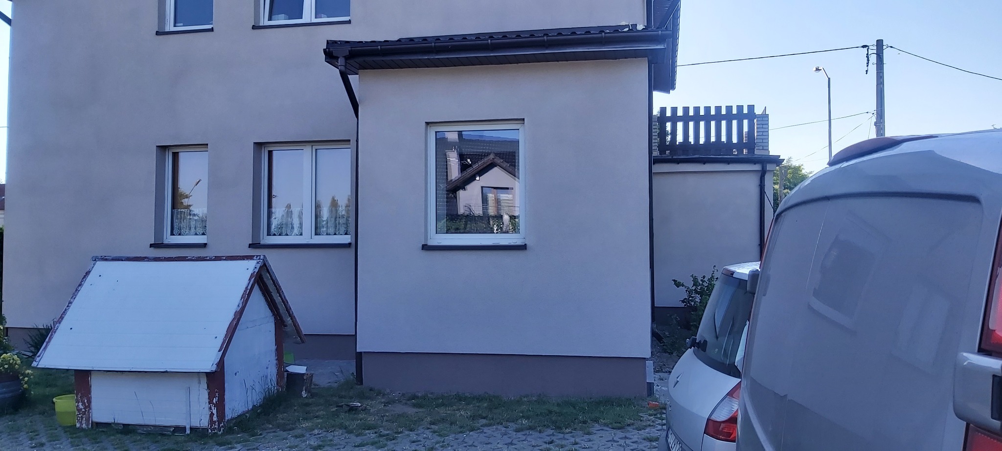 Elewacja domu jednorodzinnego po odświeżeniu, widoczny fragment zaparkowanego samochodu i buda dla psa.