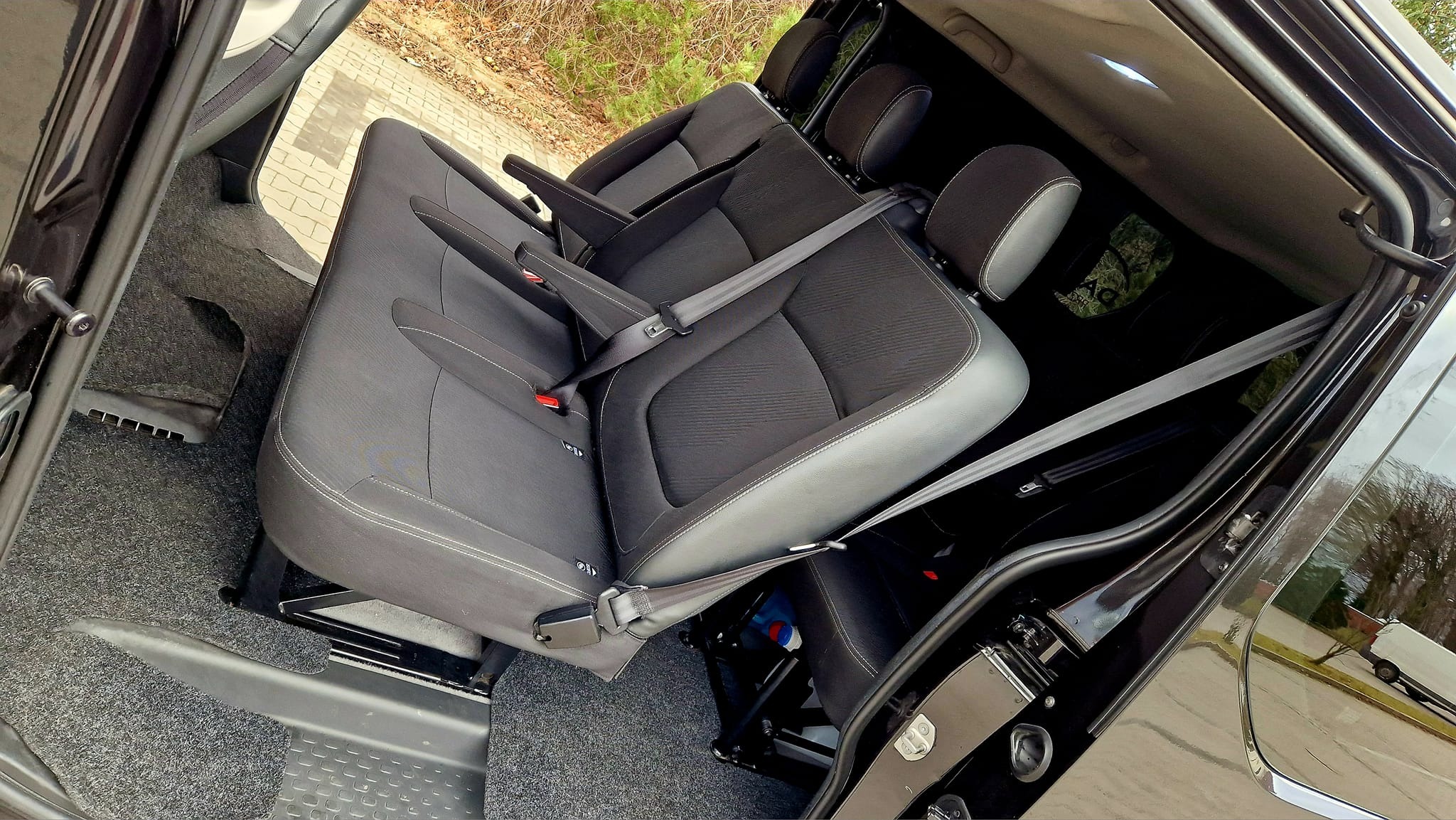 Wnętrze busa z zamontowanymi fotelami pasażerskimi, widok z perspektywy drzwi bocznych w Rosnówku. Fotele z czarną tapicerką i szarymi wstawkami, zapięte pasy bezpieczeństwa.