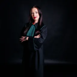 Portret kobiety w todze adwokackiej, z zegarkiem na nadgarstku, na czarnym tle.