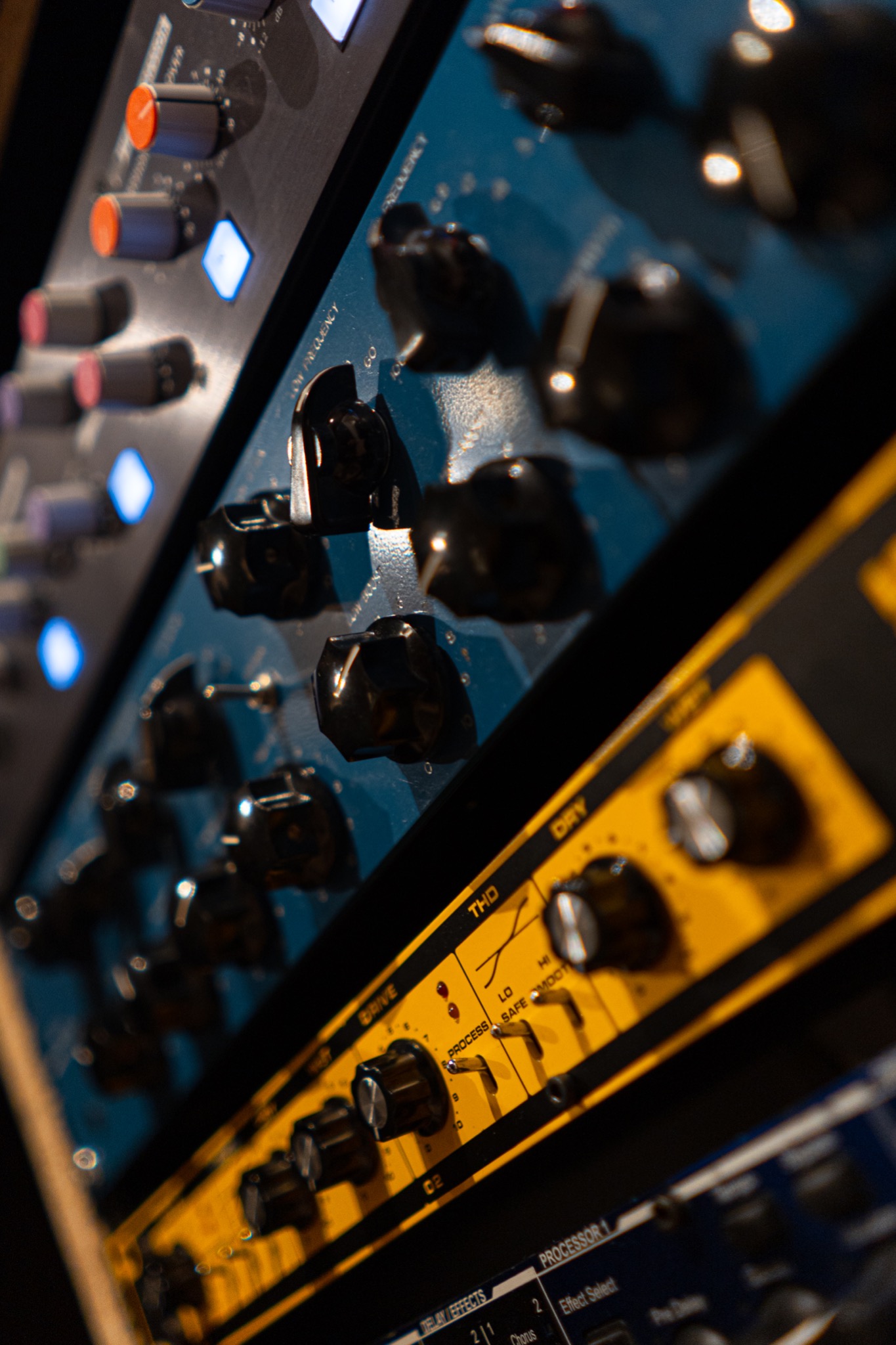 Fragment panelu mikserskiego z czarnymi pokrętłami i podświetlanymi diodami w studio nagrań, widoczne napisy 'Drive', 'THD', 'Dry', 'Frequency'.