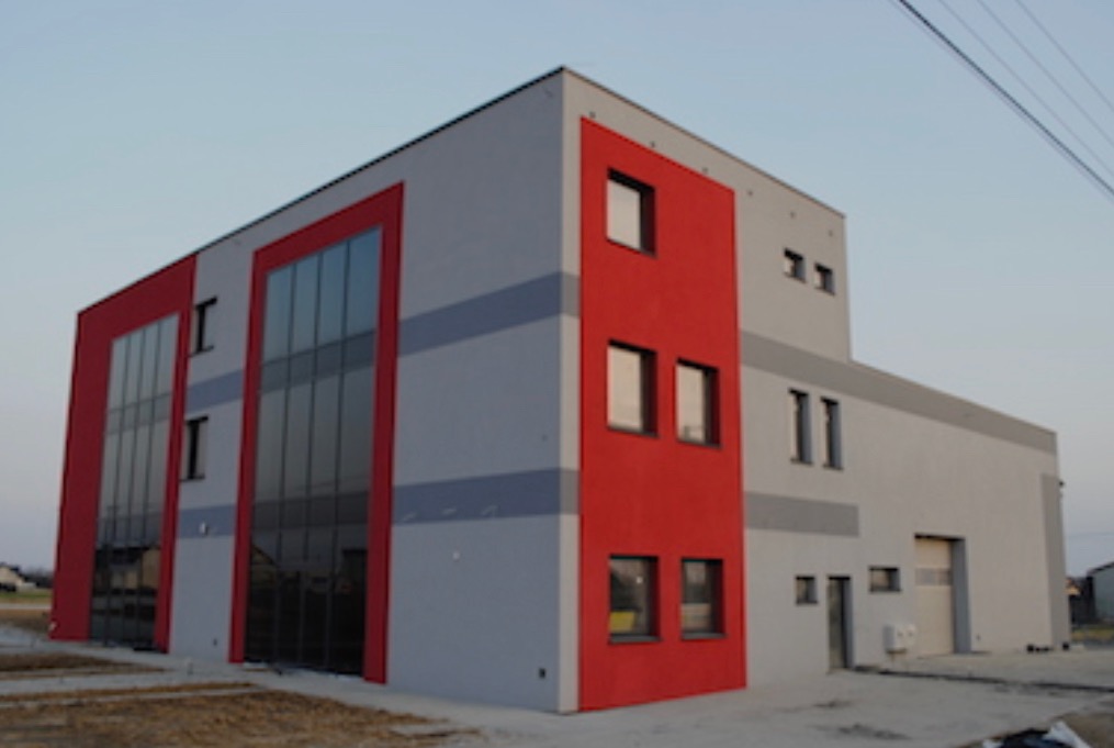 Nowoczesny budynek biurowy z szarą elewacją i czerwonymi akcentami, duże okna, widok z zewnątrz.