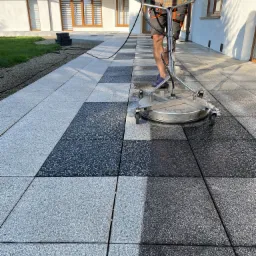 Czyszczenie kostki brukowej na tarasie przy domu z panelami słonecznymi, widoczna różnica między czystą i brudną powierzchnią.