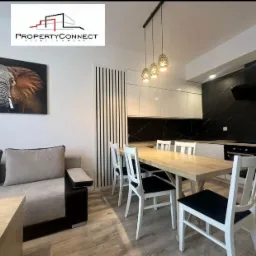 Jasne wnętrze mieszkania z sofą, stołem jadalnym i nowoczesną kuchnią z czarnym marmurem na ścianie, ozdobione obrazem słonia.