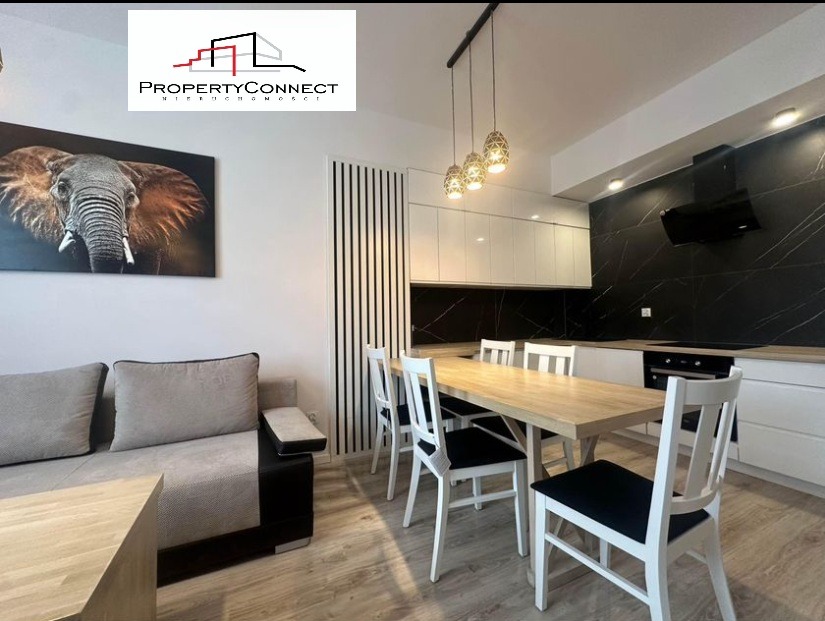 Jasne wnętrze mieszkania z sofą, stołem jadalnym i nowoczesną kuchnią z czarnym marmurem na ścianie, ozdobione obrazem słonia.