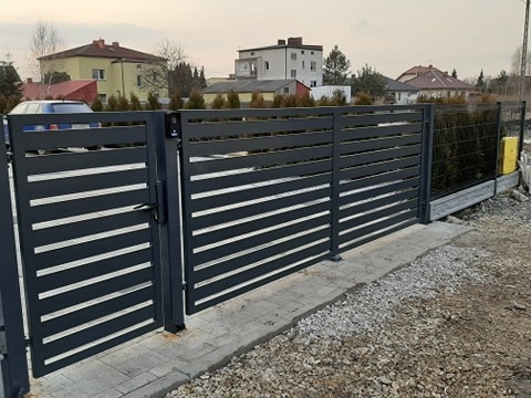 Nowoczesna brama wjazdowa i ogrodzenie panelowe w kolorze grafitowym, poziome lamele, widoczny dom w tle