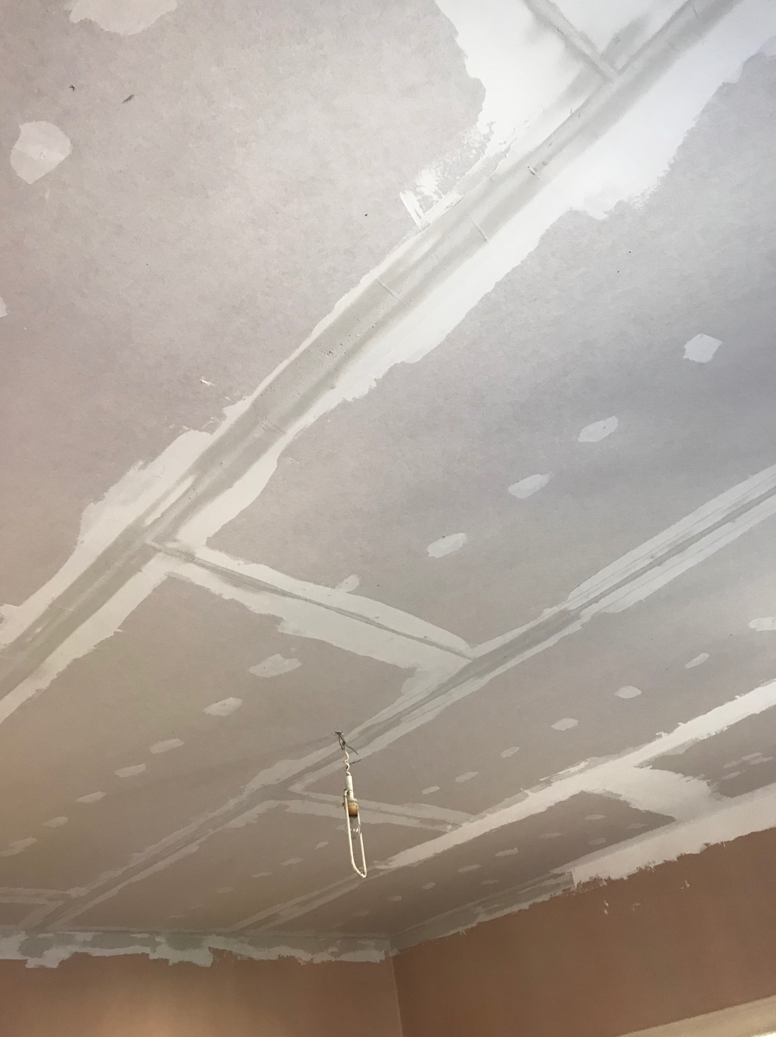 Sufit z płyt gipsowo-kartonowych po szpachlowaniu łączeń, widoczne białe pasy spoin i punktowe wypełnienia wkrętów, z zawieszonym kablem oświetleniowym.