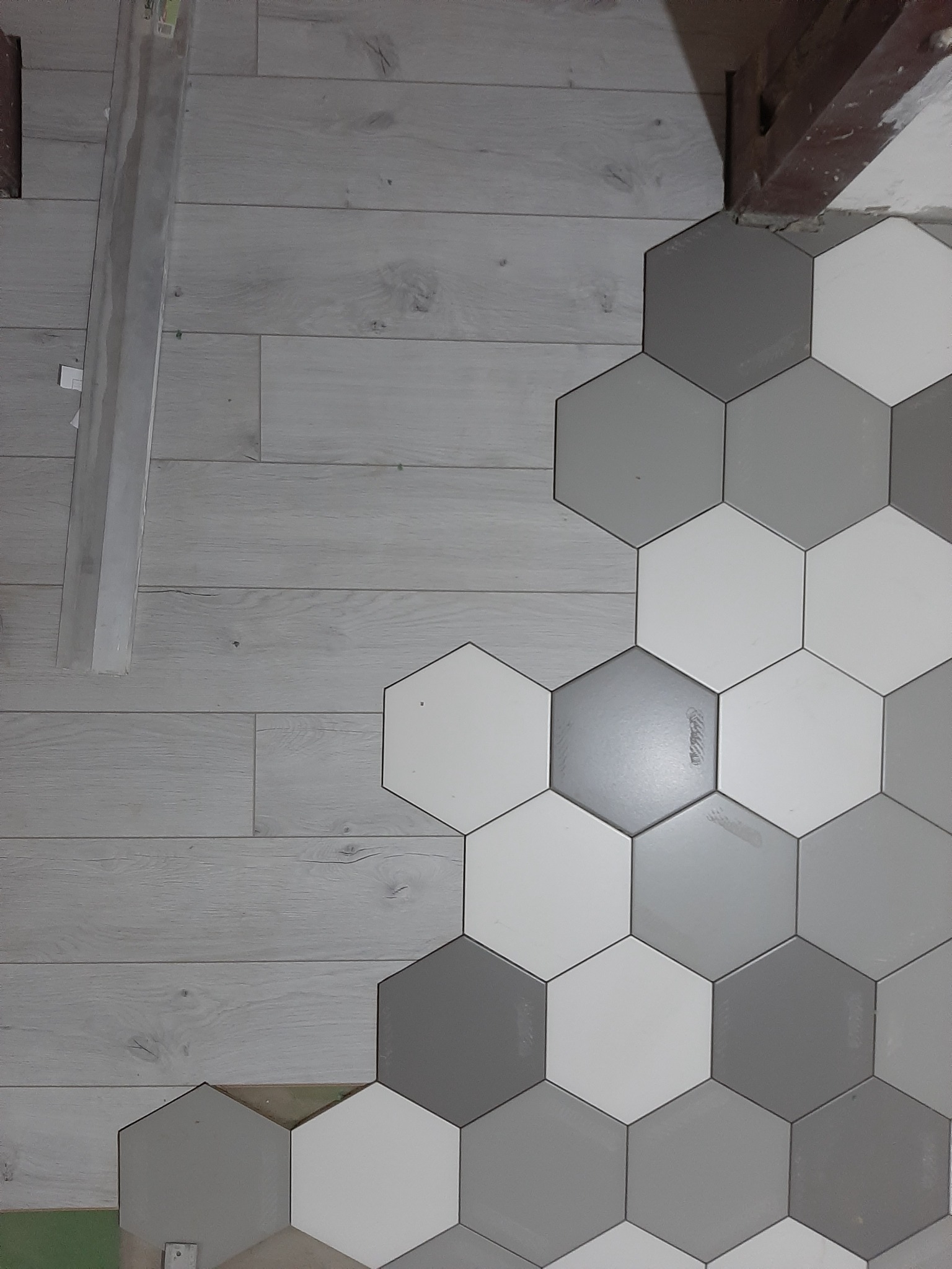 Układanie heksagonalnych płytek w odcieniach szarości i bieli na podłodze w Gdańsku, widoczne niedokończone połączenie z panelami podłogowymi.