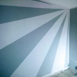 Ściana w pokoju po malowaniu z geometrycznym wzorem w odcieniach szarości i bieli, widoczne gniazdko elektryczne i listwa przypodłogowa.