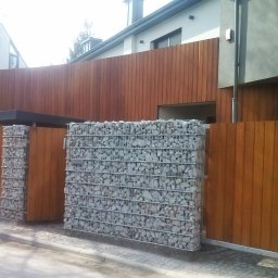 RedWood - Nowoczesne ogrodzenie z gabionów wypełnionych szarymi kamieniami, połączone z drewnianymi panelami w kolorze ciepłego brązu, tworzące estetyczną barierę wokół posesji.