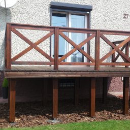 RedWood - Drewniana antresola z balustradą w stylu rustykalnym, zlokalizowana przy domu w Kalwarii Zebrzydowskiej, z widocznymi elementami wykończenia ogrodu.