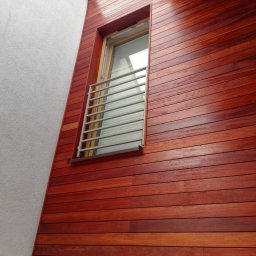 RedWood - Elewacja domu z egzotycznego drewna z oknem zabezpieczonym metalową balustradą, widok z dołu
