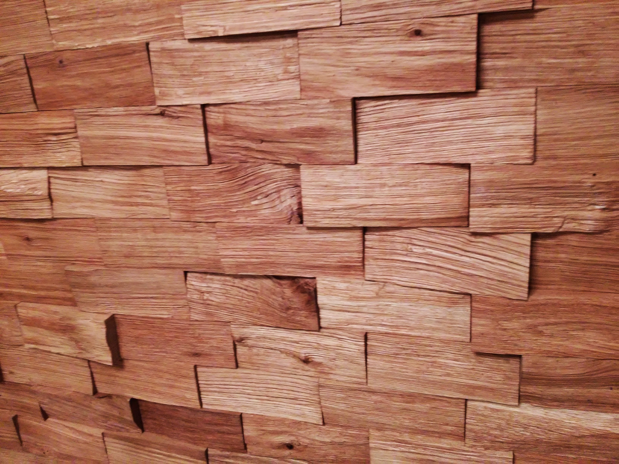 Dekoracyjna ściana z nieregularnych, drewnianych paneli o wyraźnym usłojeniu, tworzących trójwymiarowy efekt.