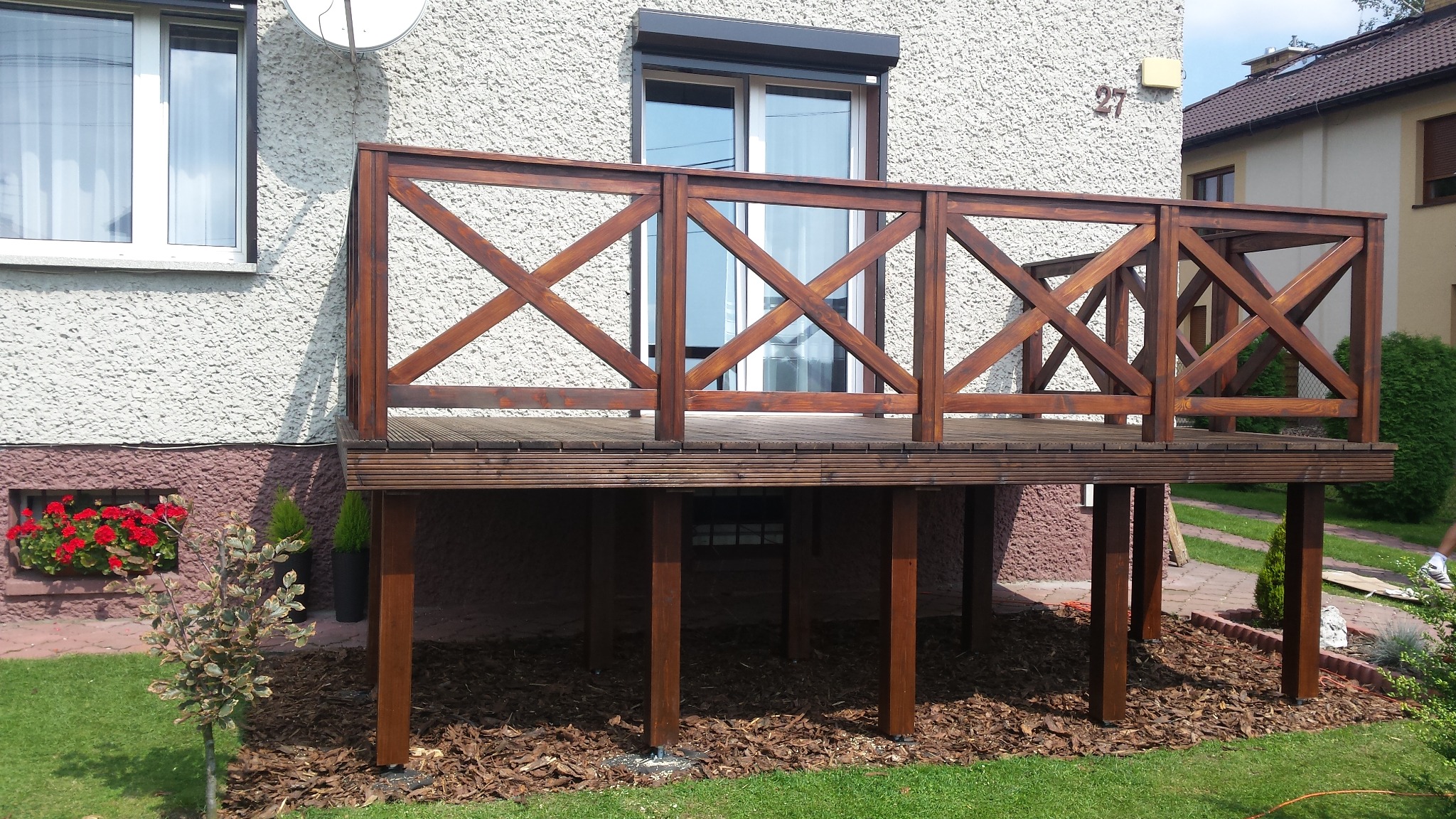 Drewniana antresola z balustradą w stylu rustykalnym, zlokalizowana przy domu w Kalwarii Zebrzydowskiej, z widocznymi elementami wykończenia ogrodu.