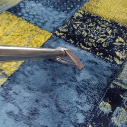 Dysza odkurzacza piorącego na tle wzorzystego dywanu w odcieniach niebieskiego i żółtego.