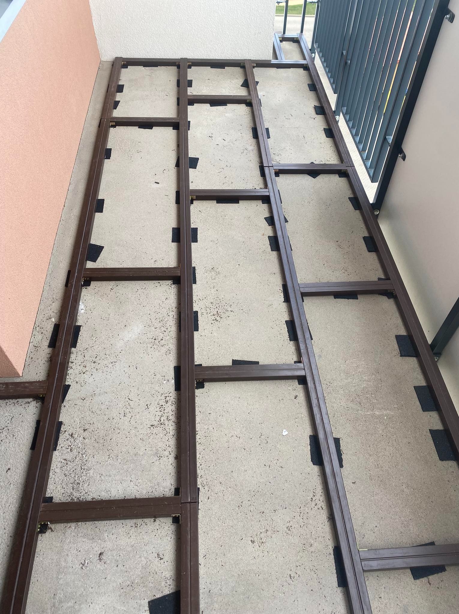 Metalowa konstrukcja pod taras na balkonie, widoczne czarne podkładki dystansowe, surowy beton pod spodem.