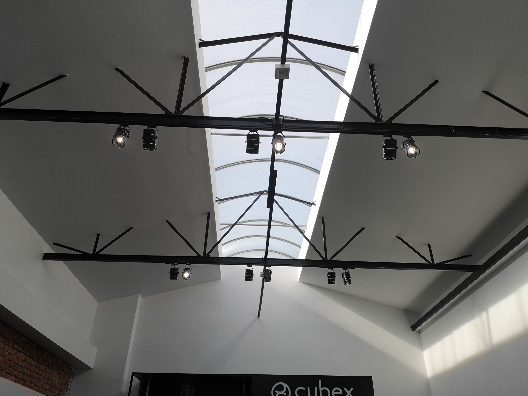 Metalowa konstrukcja sufitowa z reflektorami punktowymi i świetlikiem łukowym, widok od dołu z perspektywy pod kątem.