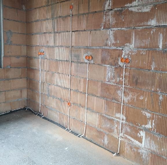 Surowy mur z cegły dziurawki z widocznymi puszkami instalacyjnymi i przewodami elektrycznymi, wstępny etap prac.