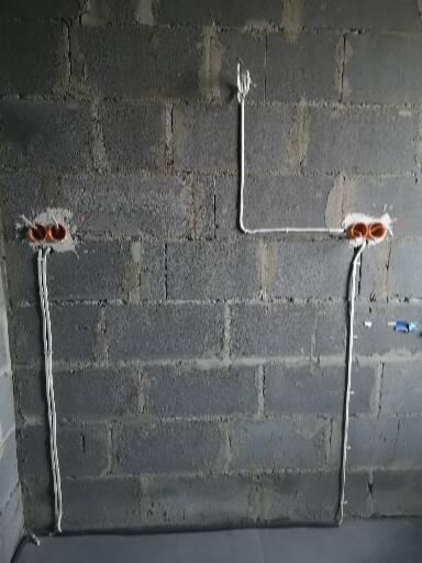 Surowa ściana z betonu komórkowego z widocznymi przewodami elektrycznymi poprowadzonymi natynkowo i puszkami instalacyjnymi w kolorze pomarańczowym.