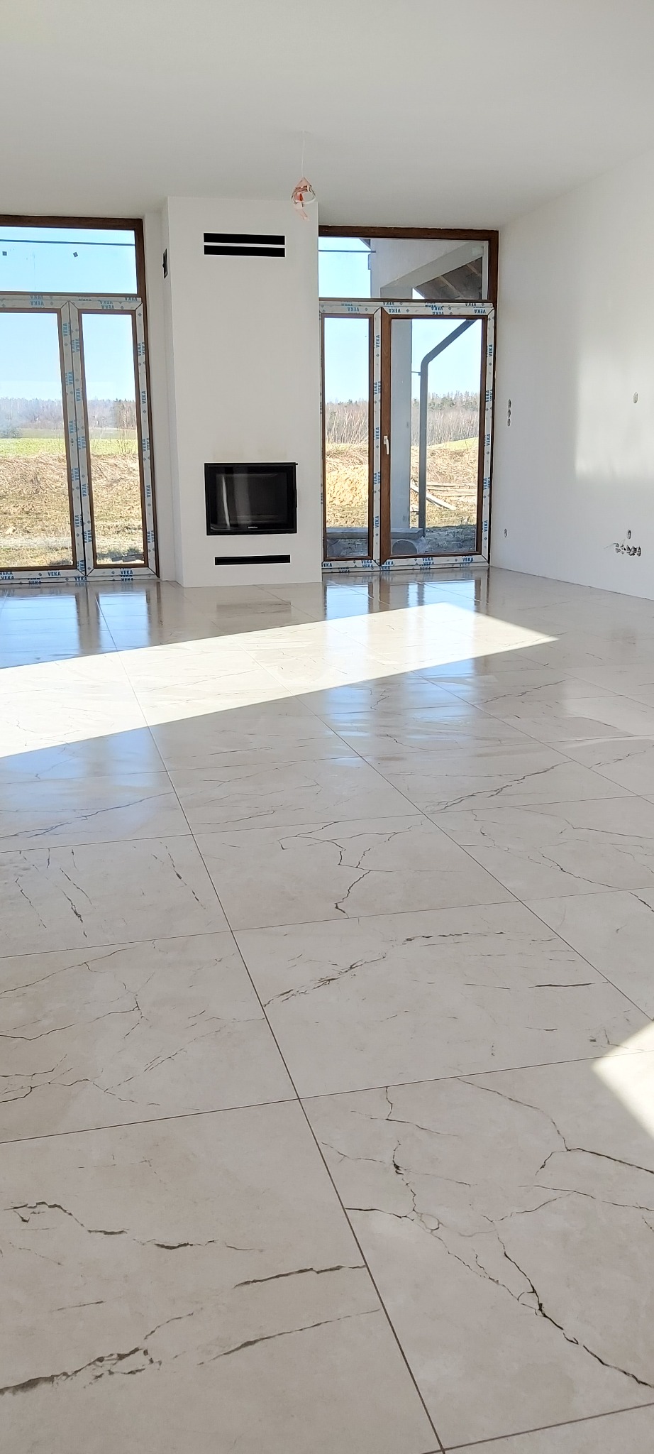 Jasne, przestronne wnętrze z nową marmurową podłogą z płytek, dużymi oknami z widokiem na zewnątrz i minimalistycznym kominkiem.