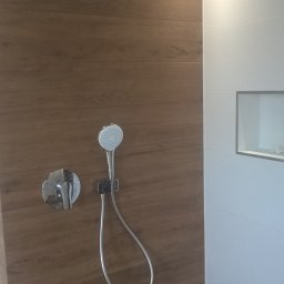 Usługi glazurnicze - Nowoczesna kabina prysznicowa z deszczownicą i słuchawką, wykończona płytkami imitującymi drewno i białymi, wbudowana półka w ścianie.