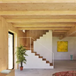 Jasne wnętrze z drewnianymi belkami stropowymi, schodami z białymi policzkami i drewnianymi stopniami, palmą w doniczce, abstrakcyjnym obrazem w odcieniach żółci i niebieskimi kaloszami przy ścianie.