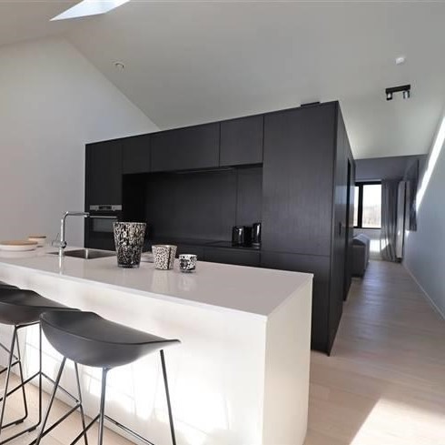 Minimalistyczna kuchnia z czarnymi szafkami i białym blatem wyspowym, trzy czarne hokery, drewniana podłoga, skandynawski styl, oświetlenie punktowe.