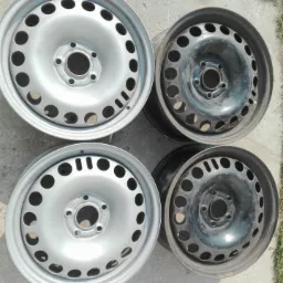 Cztery stalowe felgi samochodowe, dwie po lewej stronie w srebrnym kolorze, dwie po prawej stronie w kolorze ciemnoszarym, leżące na betonowej powierzchni w Parysowie.