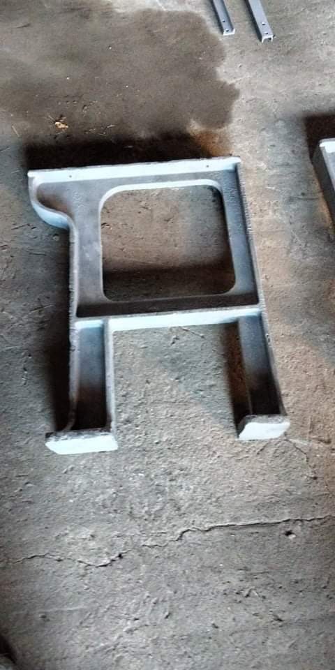 Szara, metalowa podstawa maszyny w kształcie litery A, po obróbce, leży na betonowej posadzce. Widoczne ślady obróbki i niedoskonałości powierzchni.