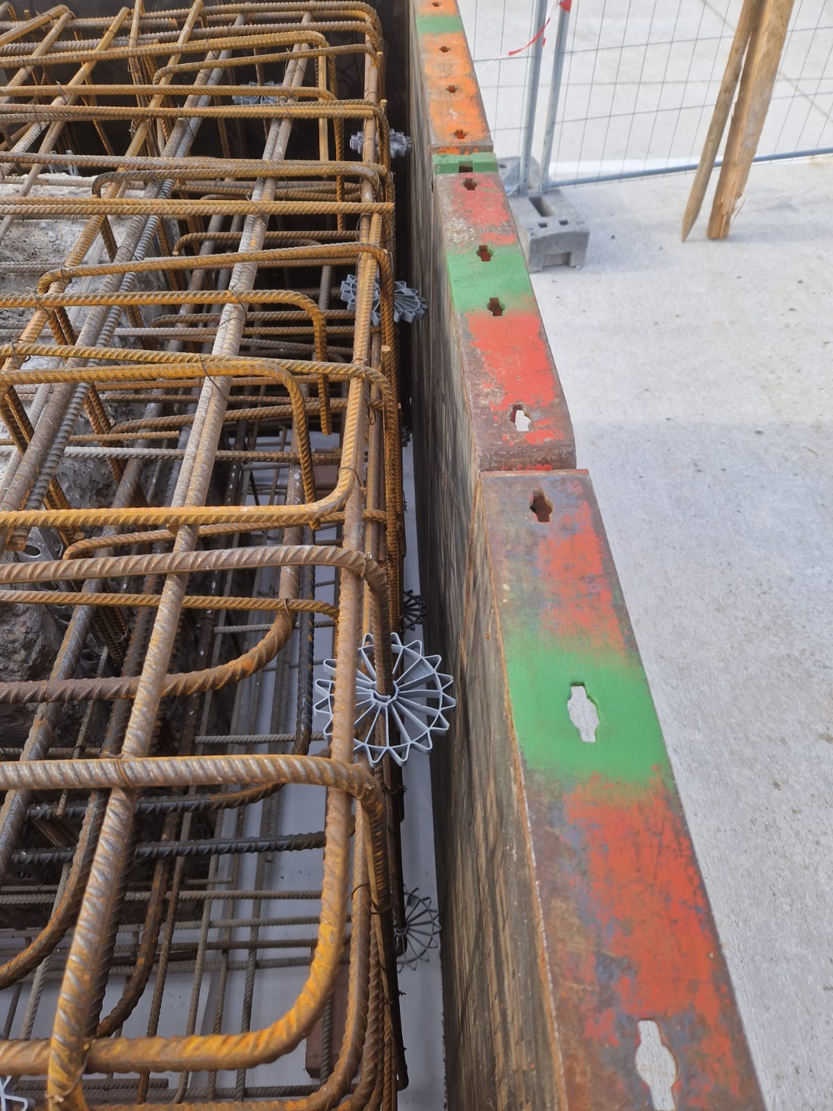 Zbrojenie fundamentów w szalunku, z użyciem dystansowych elementów z tworzywa sztucznego w kształcie gwiazdek, widoczne ślady rdzy na prętach zbrojeniowych oraz resztki betonu.