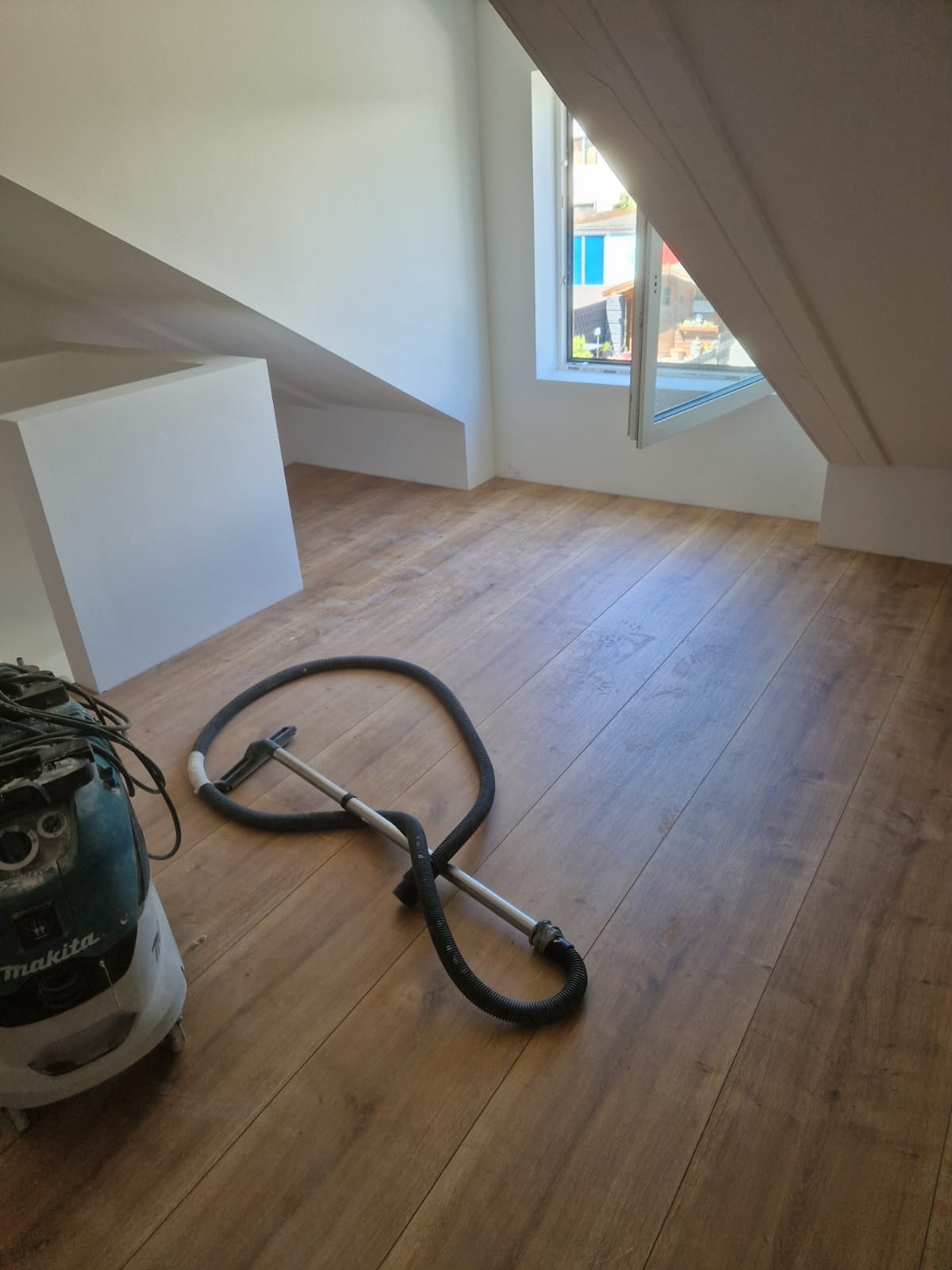 Poddasze po remoncie z nową podłogą z paneli, widoczny odkurzacz przemysłowy Makita i fragment okna dachowego.