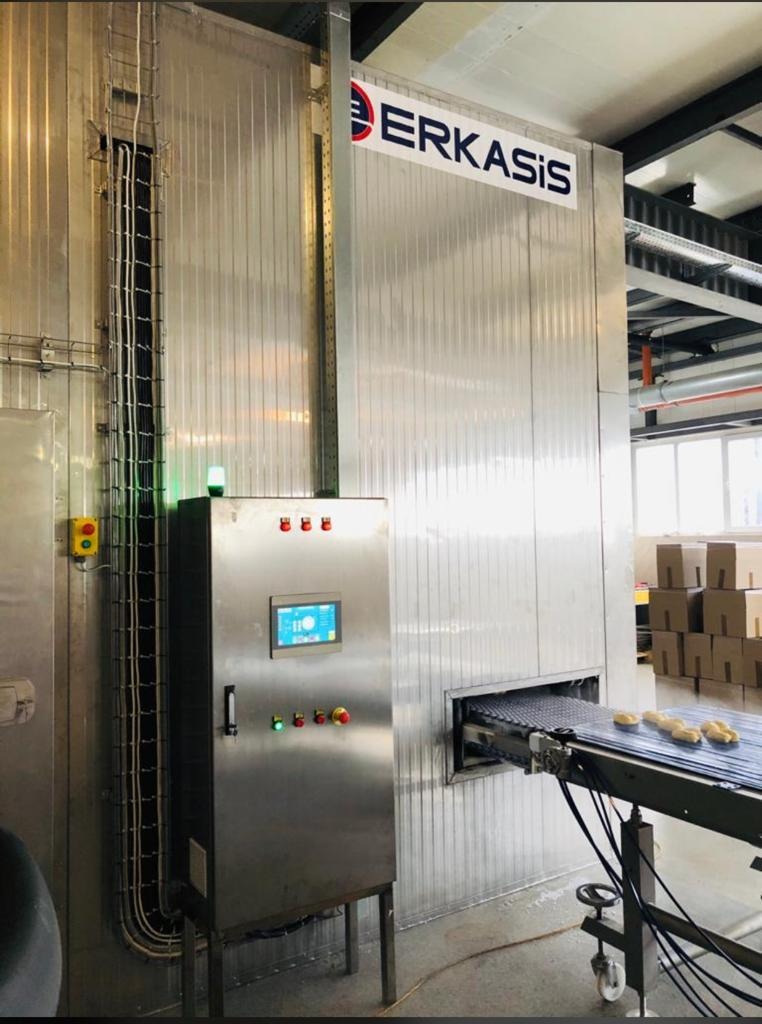 Przemysłowa instalacja z logo ERKASIS, prawdopodobnie tunel chłodniczy, z panelem sterowania i taśmą transportującą produkty spożywcze.