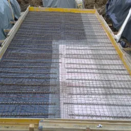 Przygotowanie zbrojenia i izolacji pod wylewkę fundamentową w szalunku drewnianym, widoczne folie izolacyjne i siatka zbrojeniowa.