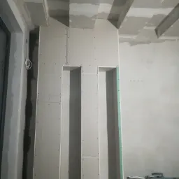 Konstrukcja z płyt gipsowo-kartonowych tworząca wnęki w ścianie, widoczne profile metalowe na podłodze, surowy stan wykończenia wnętrza.