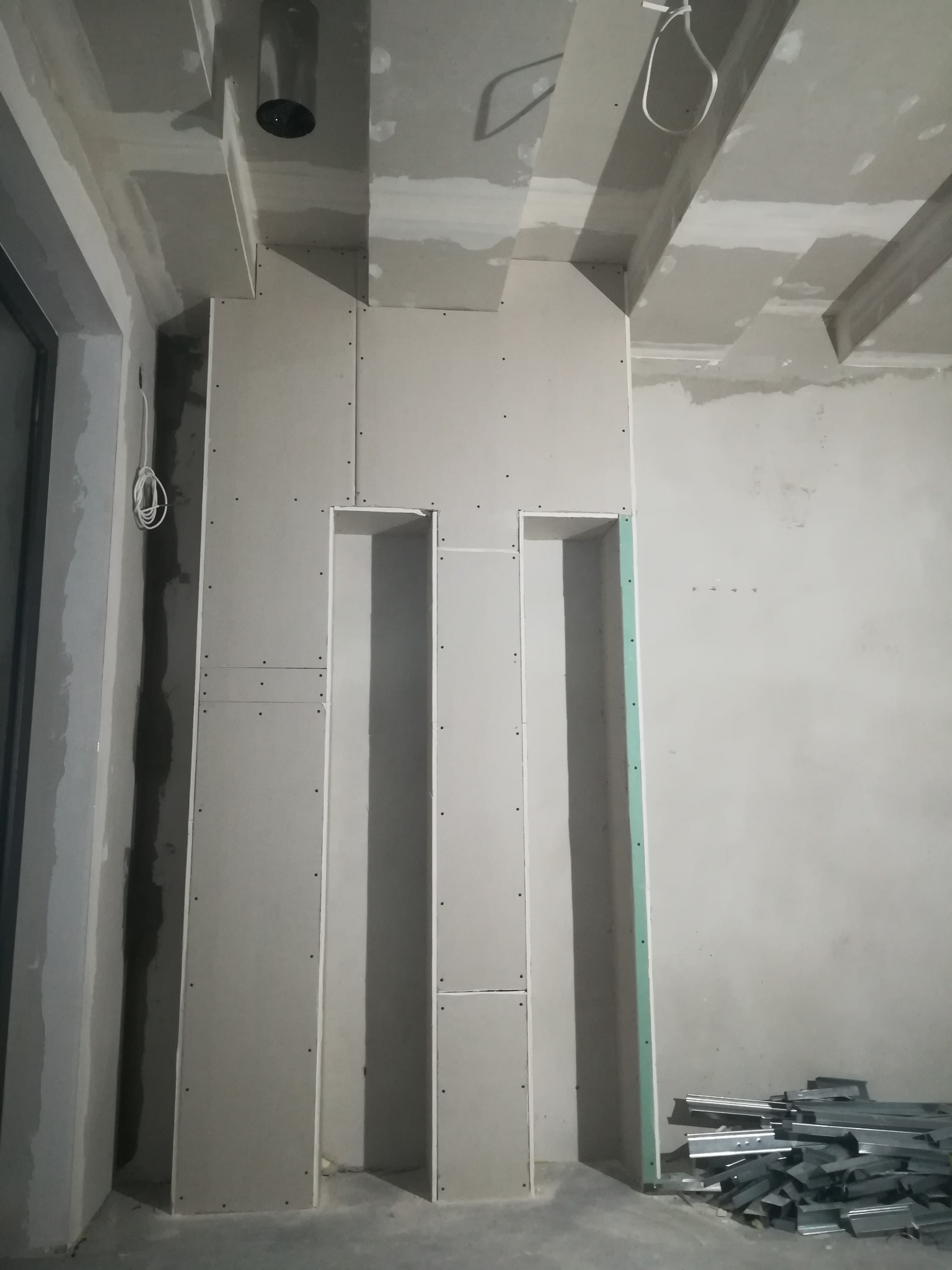 Konstrukcja z płyt gipsowo-kartonowych tworząca wnęki w ścianie, widoczne profile metalowe na podłodze, surowy stan wykończenia wnętrza.