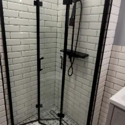 Nowoczesna kabina prysznicowa narożna z czarnymi profilami, białe płytki typu metro i wzorzysta podłoga, widok z góry.