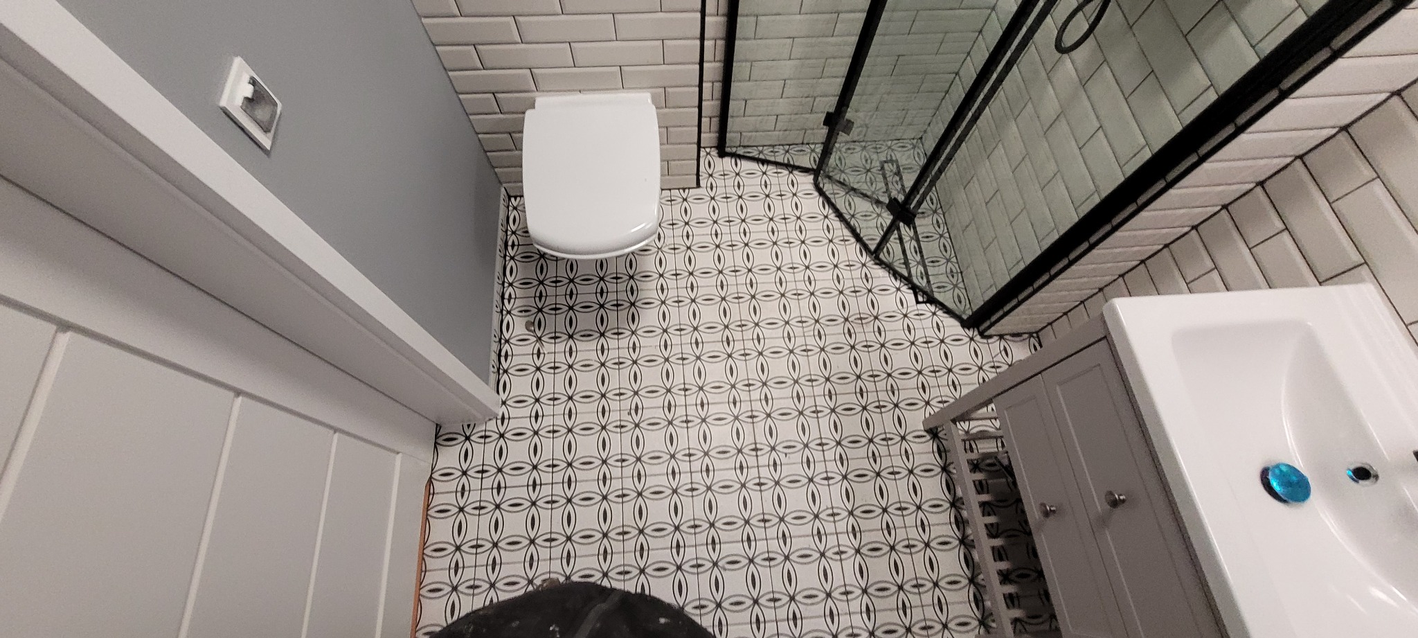 Wykończona łazienka w Pisz z białą armaturą, kabiną prysznicową z czarnymi ramami i wzorzystą podłogą, sfotografowana z góry.