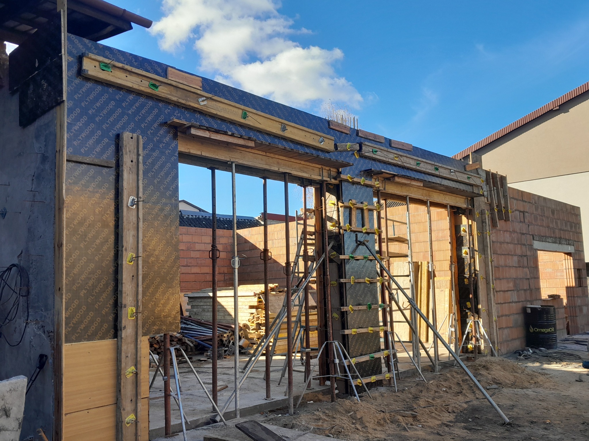 Szlifowanie betonu z użyciem szalunków systemowych i podpór teleskopowych, widok na nieukończone ściany z cegły i błękitne niebo.