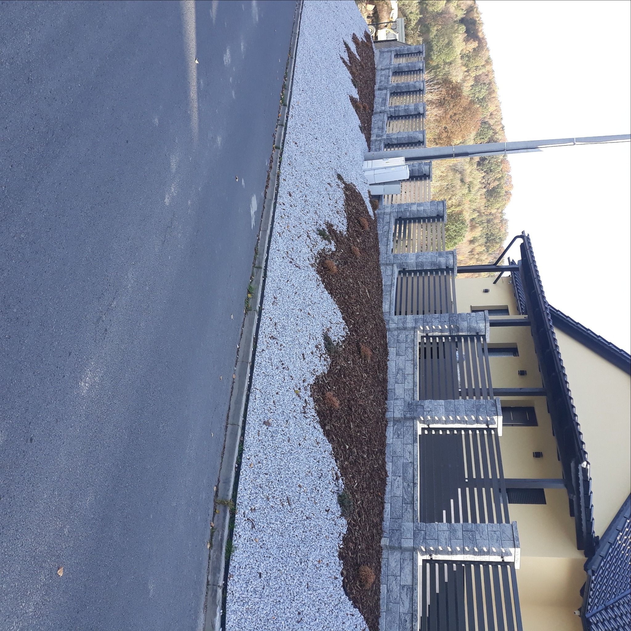 Nowoczesny ogród przydomowy z jasnym żwirem, korą i ozdobnym ogrodzeniem z elementami z szarej kostki, widok z góry na posesję.