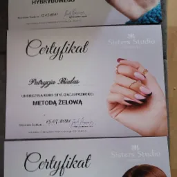 Trzy certyfikaty ukończenia kursów stylizacji paznokci (manicure hybrydowy i metodą żelową) oraz kursu podstawowego makijażu, opatrzone logo Sisters Studio kosmetyka.