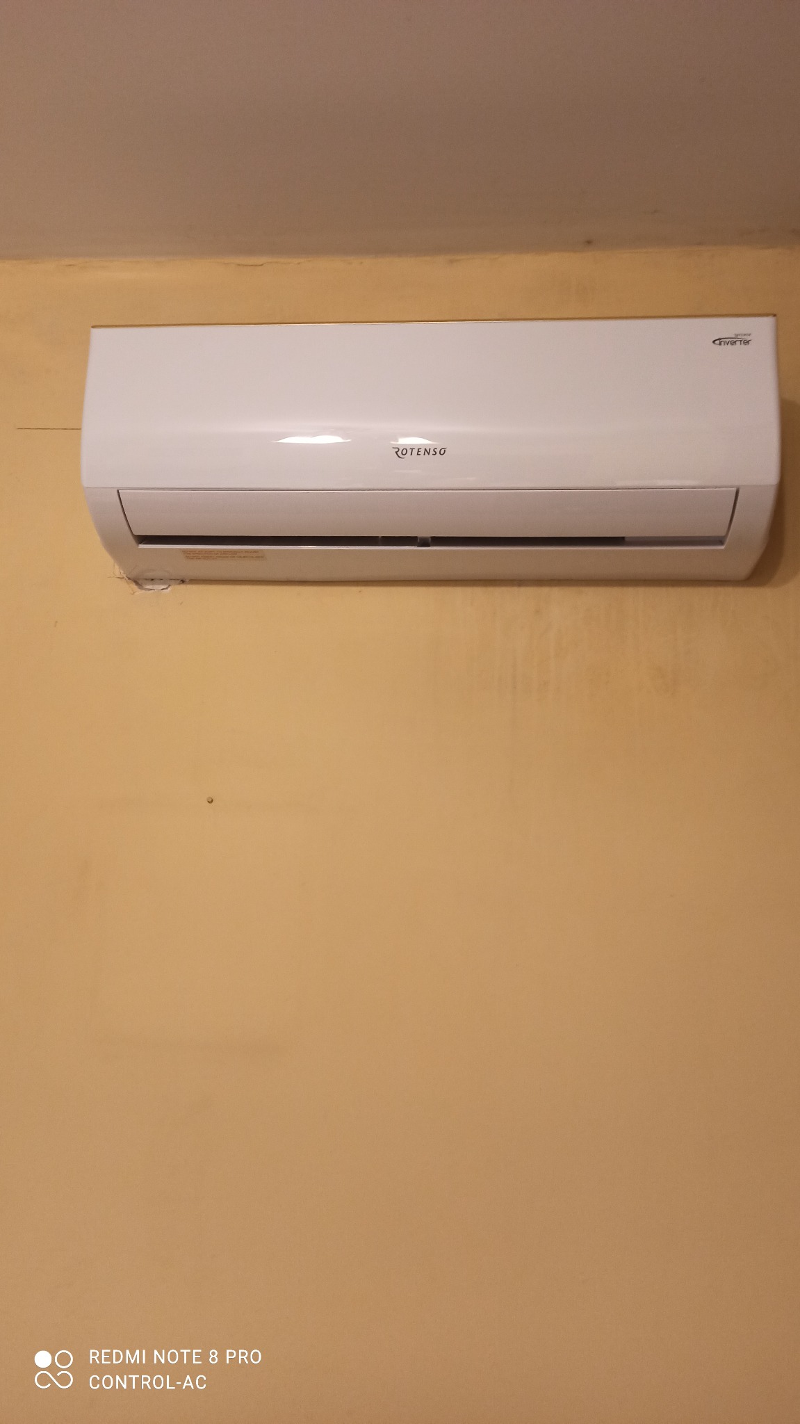 Biały klimatyzator marki Rotenso zamontowany na żółtej ścianie w pomieszczeniu.