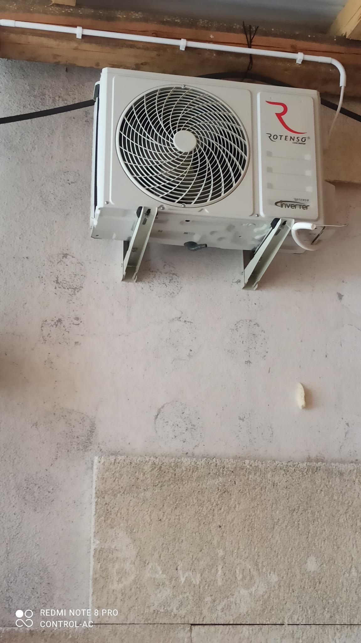 Biała jednostka wewnętrzna klimatyzatora Rotenso zamontowana na ścianie z widocznymi śladami po poprzednich instalacjach i elementami instalacji elektrycznej pod sufitem.