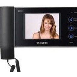 ROBKAM SERVICE Robert Kołak - Czarny wideodomofon Samsung z kolorowym wyświetlaczem prezentującym uśmiechniętą kobietę, zamontowany na białej ścianie z widocznym kablem spiralnym.