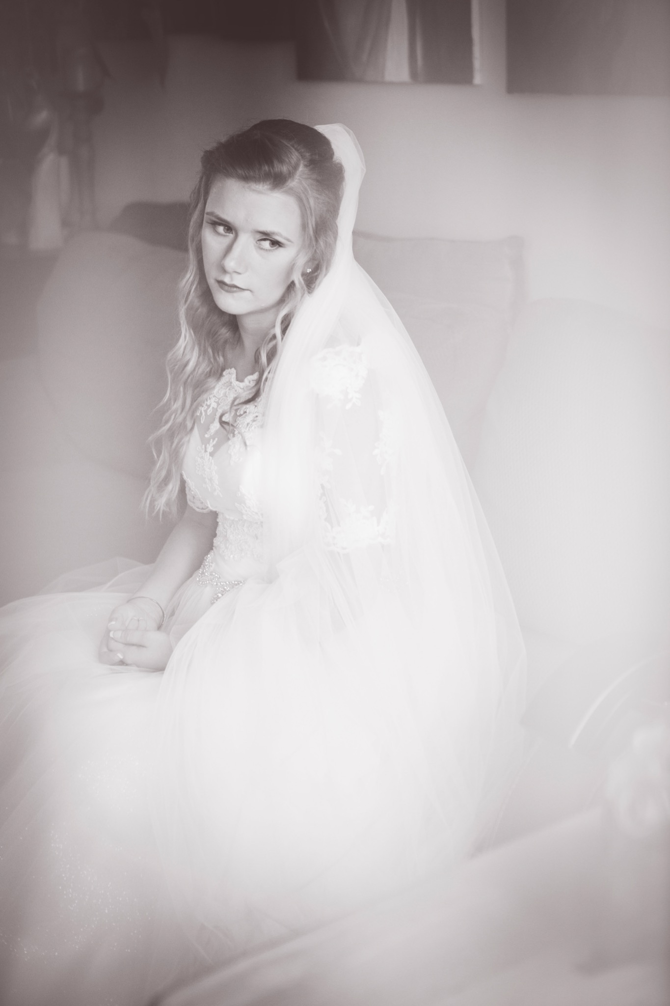 Portret panny młodej w sukni ślubnej i welonie, siedzącej na sofie, z zamyślonym spojrzeniem skierowanym w lewo, w sepii.